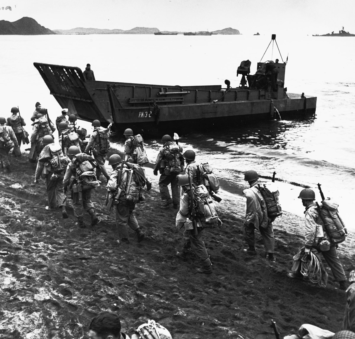 1200px-Troops_marching_up_beach_during_loading_for_Kiska_operation,_13_August_1943_(80-G-475421)